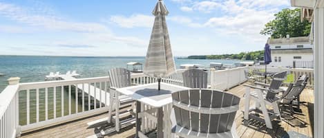 A wooden deck with outdoor furniture, including chairs and tables, overlooking a body of water.