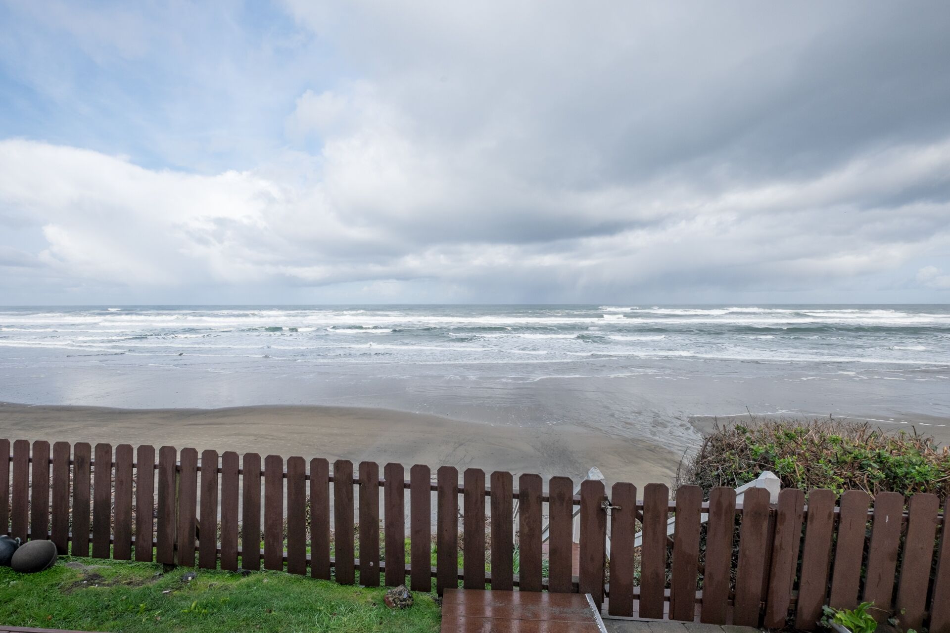 A beach view with a wooden fence in the foreground.