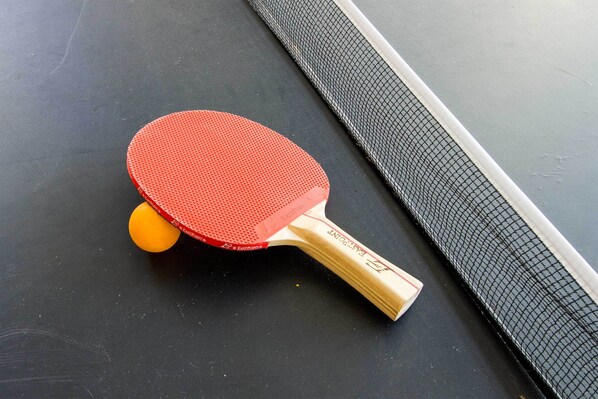 Taula de ping-pong amb una xarxa, una paleta vermella de tenis taula i una pilota groga.