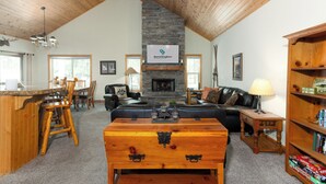 A spacious living area with a stone fireplace, wooden furniture, and a cozy fireplace mantel. - TIMB03 - Classic Lodge Style Home, Single Level, Ping Pong & Foosball, Hot Tub (Sunriver)