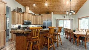 A spacious kitchen with wooden cabinets, a stainless steel refrigerator, and a bar area with wooden stools. - TIMB03 - Classic Lodge Style Home, Single Level, Ping Pong & Foosball, Hot Tub (Sunriver)