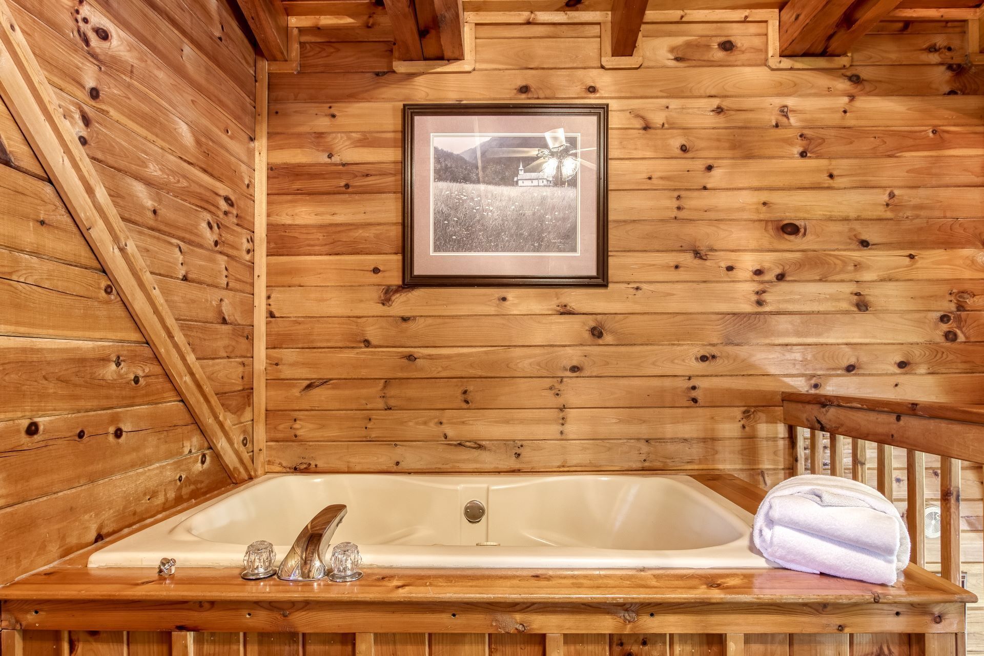 Interior de una cabaña de madera con una bañera de madera, una fotografía en el marco en la pared y una toalla en el borde de la bañera.