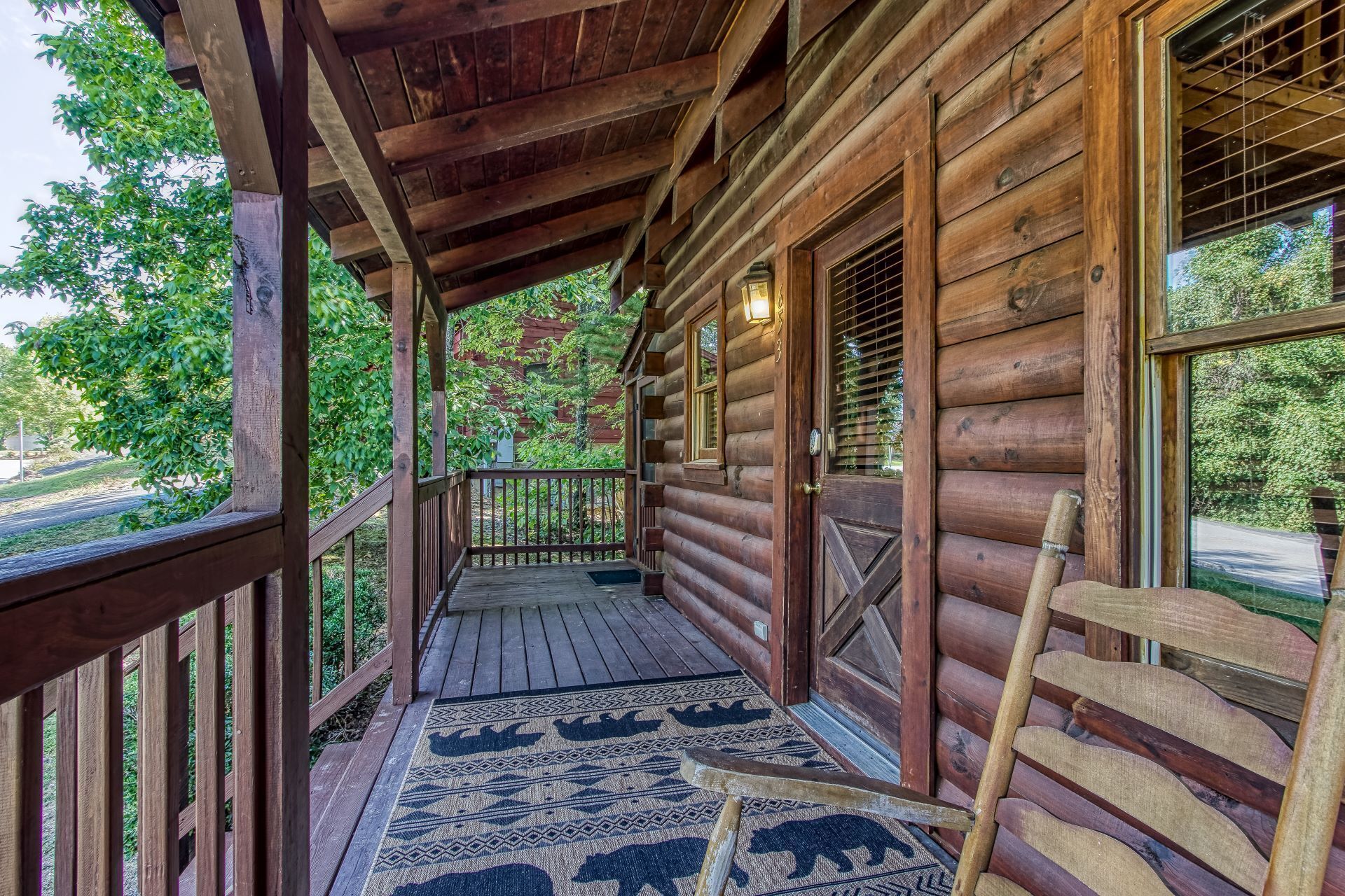 A wooden cabin with a porch, a wooden bench, and a rug with bear designs.