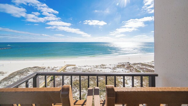 A balcony with wooden chairs overlooking a beach with clear blue water and a bright sun. - 3 BR 2 BA ~ Phoenix East ~ See why our guests chose us! *BeachFront!* (Orange Beach)