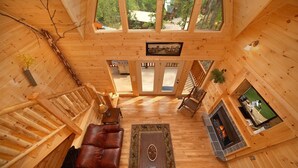 Interior de cabana de madeira com lareira, sofá de couro, mesa de jantar e televisão.