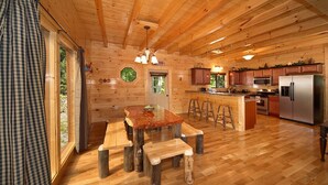 Interior de uma cabana de madeira com cozinha, área de refeições e uma grande janela.