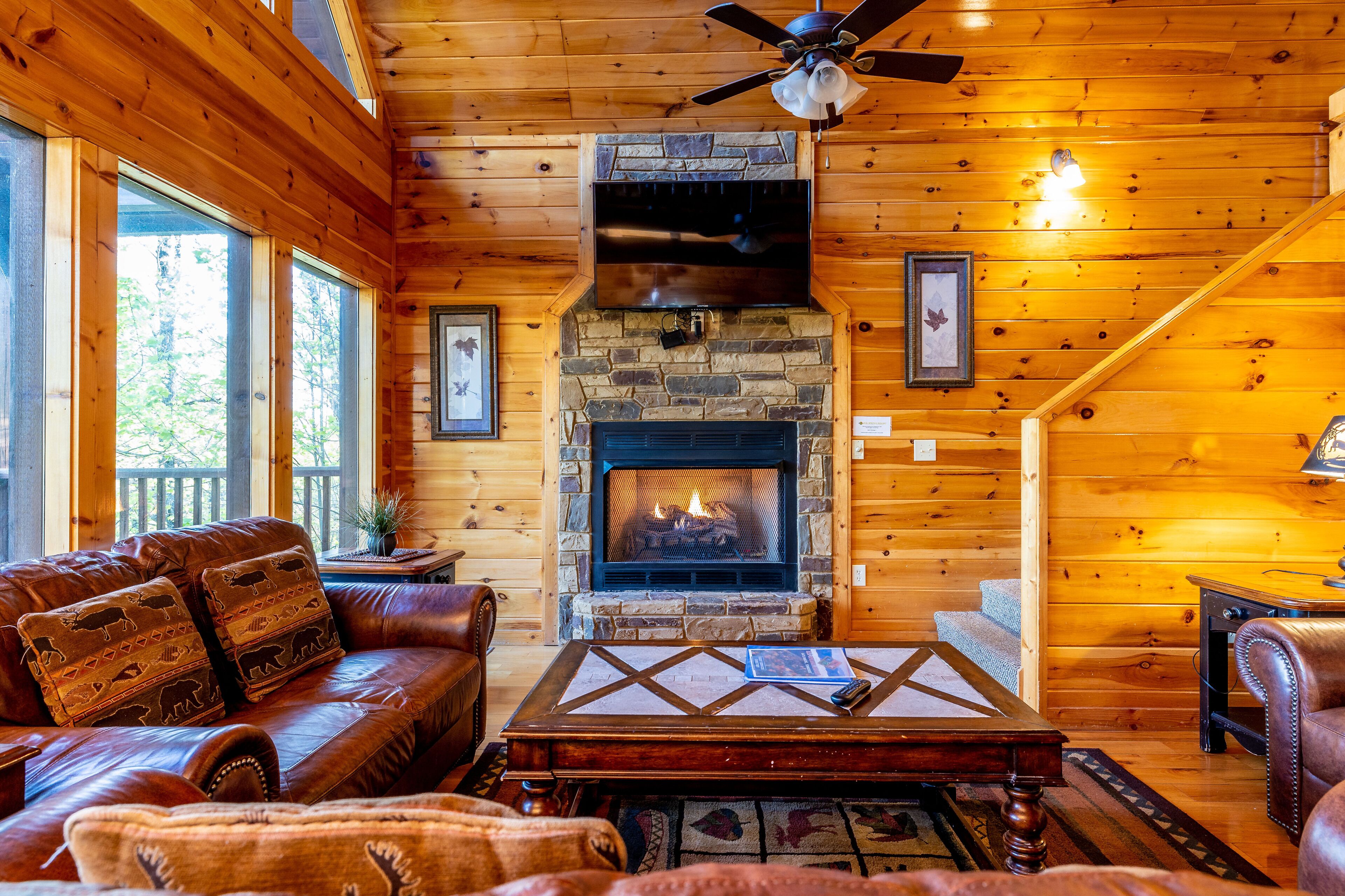 A cozy cabin interior with a stone fireplace, leather furniture, and wooden walls.