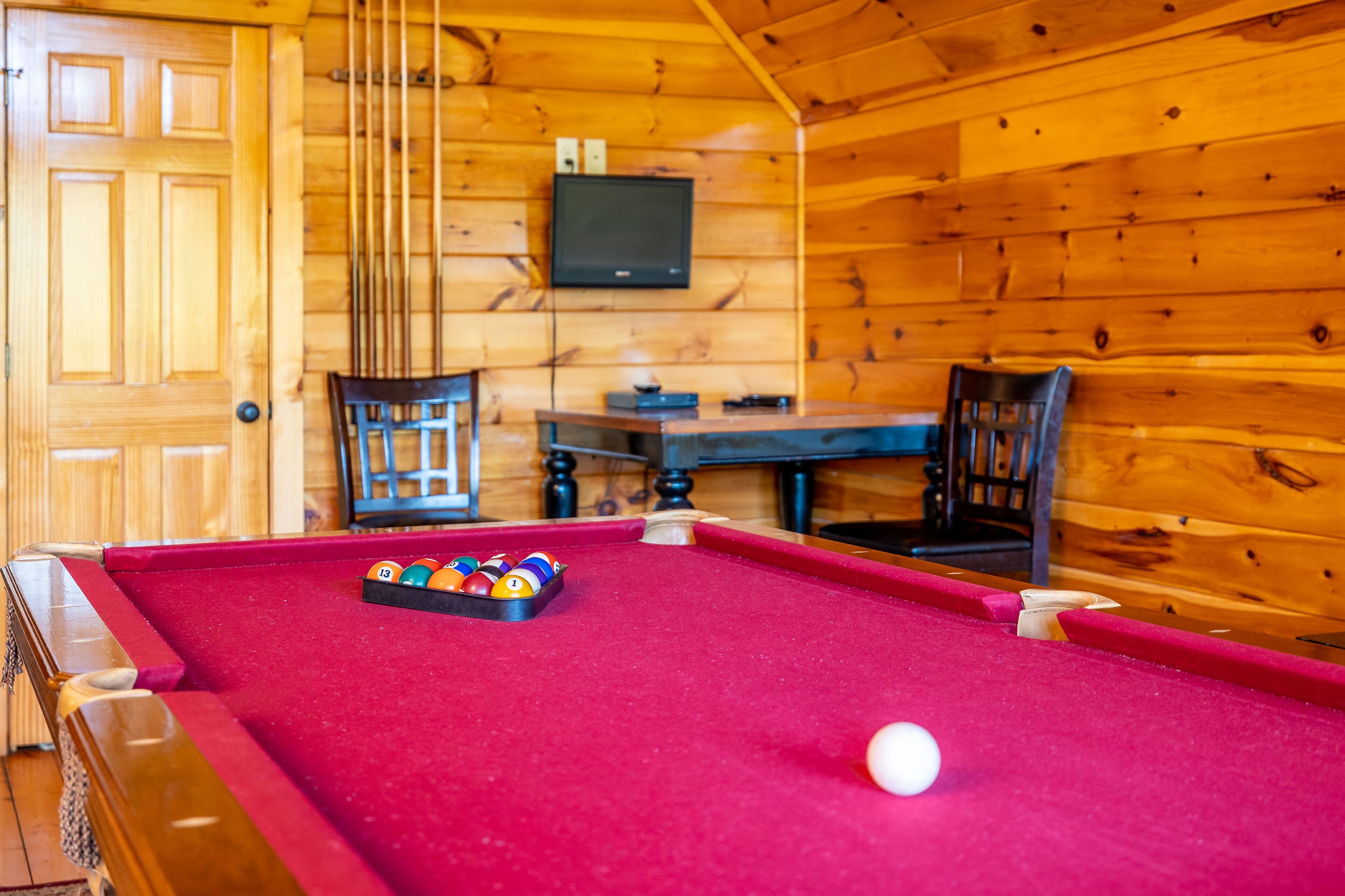 A pool table with balls, a television mounted on the wall, and wooden walls.