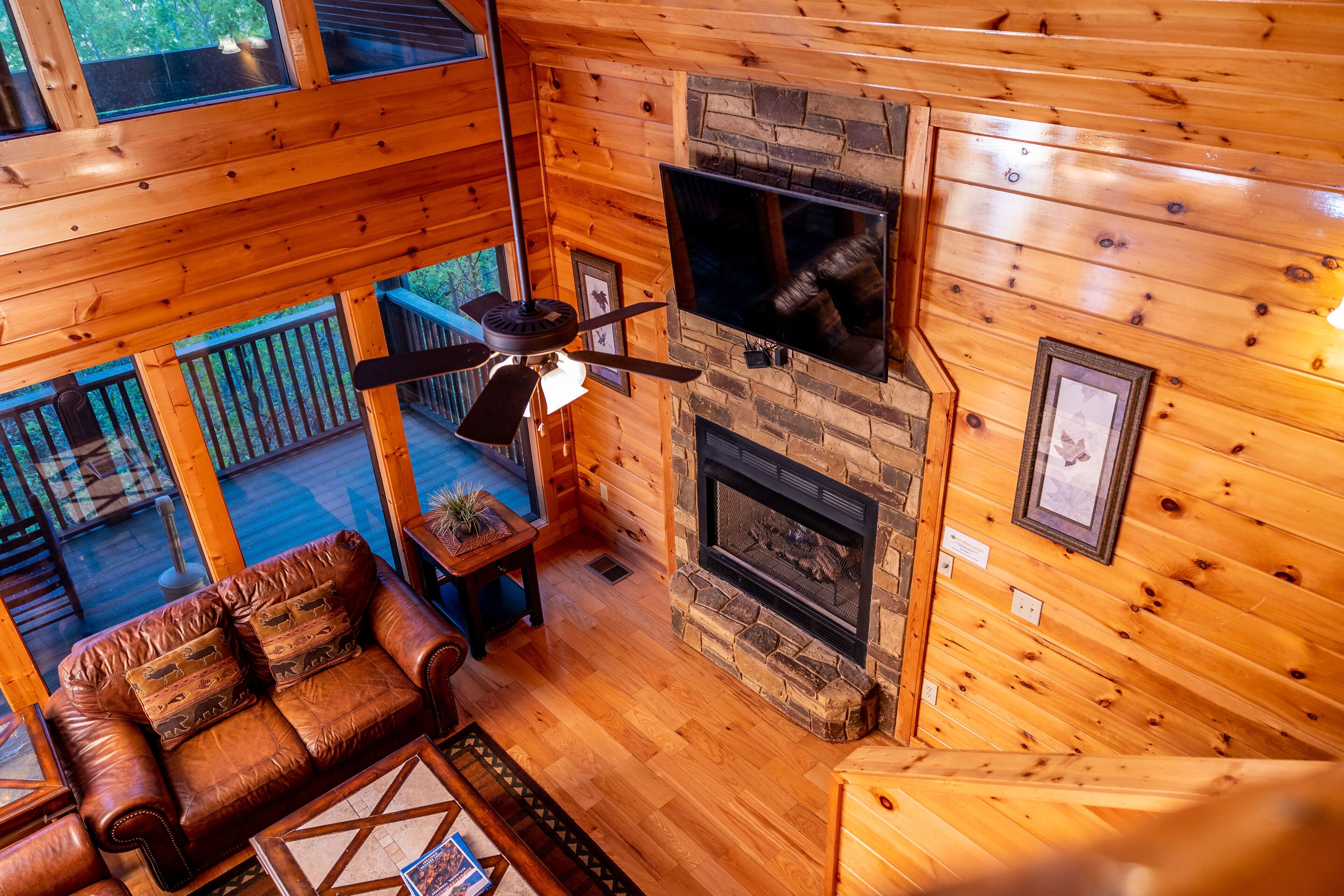 Interior de una cabaña de madera con chimenea de piedra, ventilador de techo y sofá de cuero.