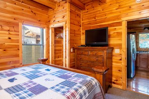 Camera da letto in una baita di legno, con un letto, una televisione, un comò e un frigorifero.
