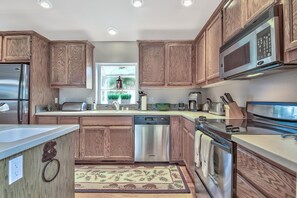 Cozinha moderna com armários de madeira, eletrodomésticos de aço inoxidável e uma janela com vista para o verde.