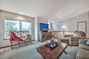 Uma sala de estar com uma grande janela, um banco de madeira, um sofá, uma mesa de centro e uma televisão.