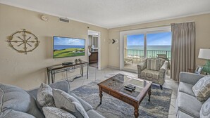 Ein Wohnzimmer mit großem Fernseher, Couchtisch und Sofa. Ein Balkon bietet Blick aufs Meer.