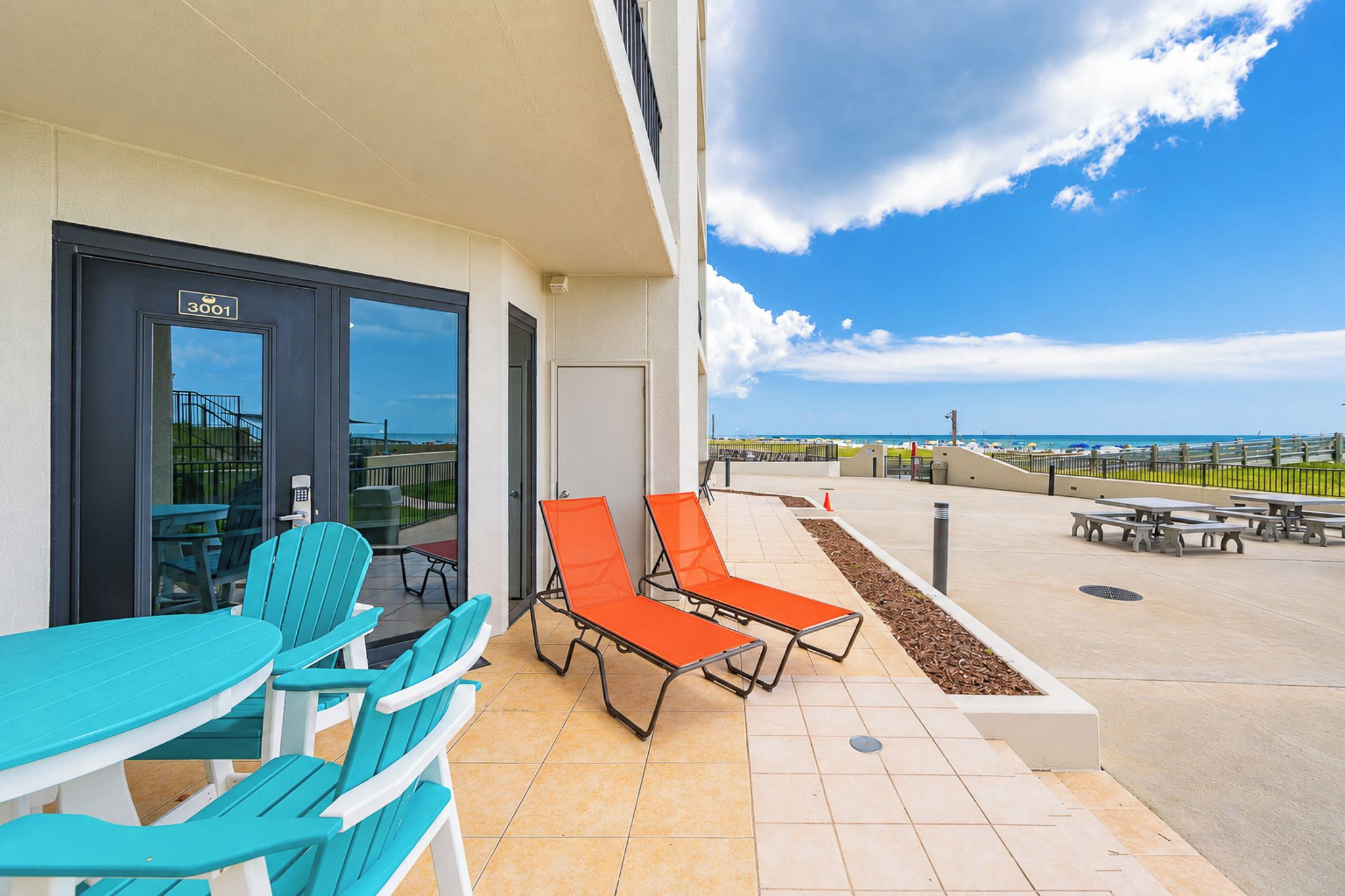 Un balcon avec des sièges d’extérieur, une vue sur la plage et l’entrée de l’immeuble.
