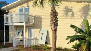 A two-story house with a balcony, a palm tree, and a garden with various plants.