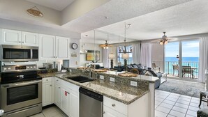 A modern kitchen with granite countertops, white cabinets, and stainless steel appliances. It features a large island with a sink, and a dining area with a view of the ocean.
