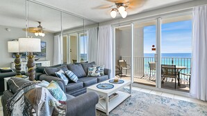 A modern living room with a gray sofa, a coffee table, and a balcony with a view of the ocean.