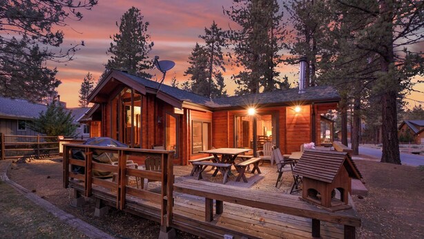 Una cabaña de madera con terraza, mesa de picnic y sillas.