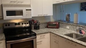 Una cocina con armarios blancos, horno de acero inoxidable, microondas, tostadora y pileta.