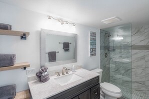 A modern bathroom with a glass shower enclosure, a large mirror, and a vanity with a sink and countertop.