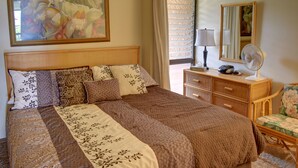 Un letto rifatto con una coperta a fantasia, un comodino con una lampada, uno specchio e una sedia in vimini.