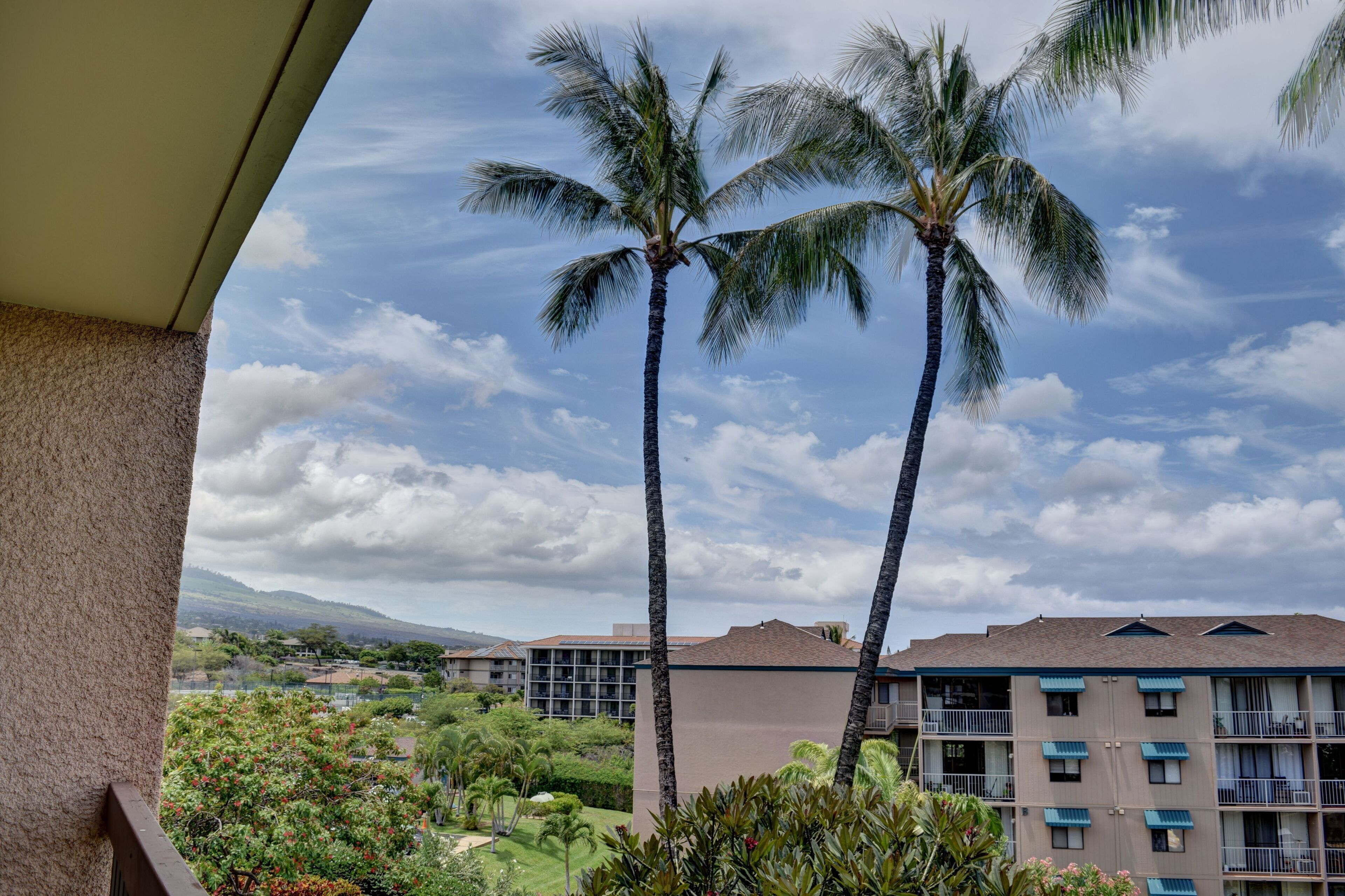 A hotel with a balcony overlooking palm trees and a view of other buildings.