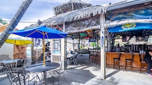 Un área de bar al aire libre con sombrillas de estilo tiki, sillas de metal y una barra.
