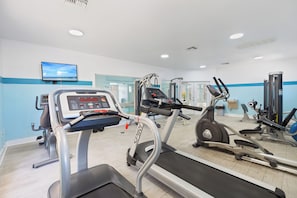 Une salle de sport équipée de tapis de course, d’un vélo d’appartement et d’appareils de musculation.