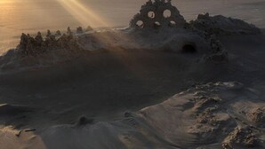 A beach with a large sand structure and a person in the distance.