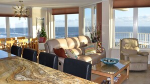 A spacious living room with a large glass table, leather sofa, and a view of the ocean.
