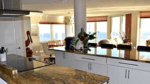 A modern kitchen with granite countertops, white cabinets, and a view of the ocean through large windows.