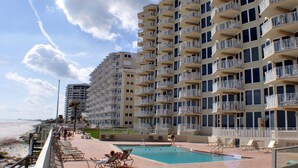 A beachfront hotel with multiple balconies, a swimming pool, and sun loungers.