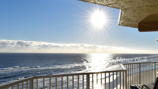 A balcony with a view of the ocean and the sun shining through the clouds.