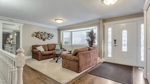 Ein Wohnzimmer mit zwei braunen Sofas, einem Couchtisch und einem Teppich. Eine Treppe mit weißen Geländern führt zu einer weiteren Ebene.