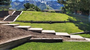 Ein gepflegter Rasen mit einer Holztreppe, die zu einem Gebäude führt, umgeben von Bäumen und Bergen im Hintergrund.