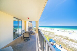 A balcony with a table and chairs, overlooking a beach with umbrellas and people.