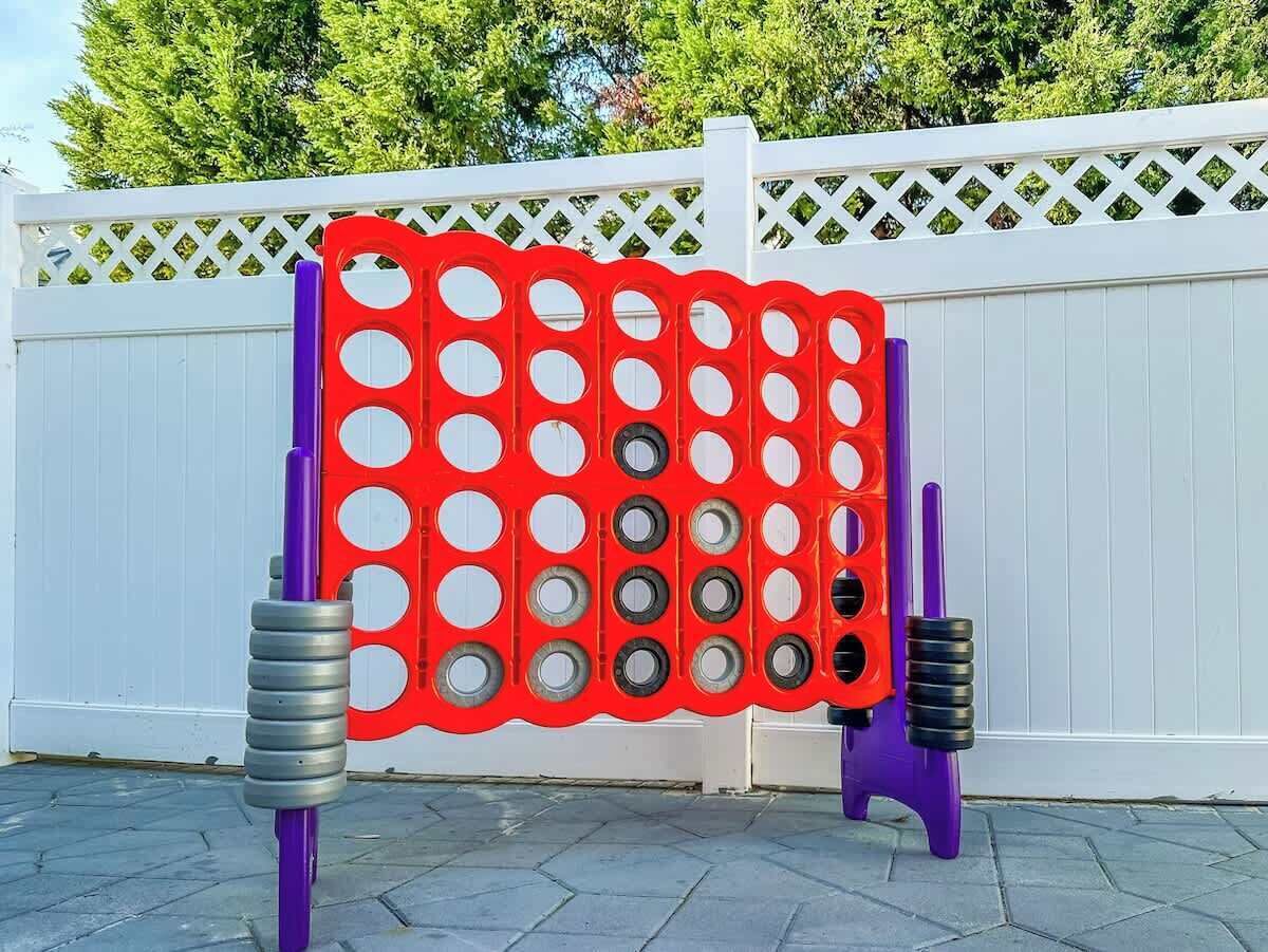 Eine Spielgeräte-Konstruktion in Rot und Violett mit runden Löchern und Metallringen, vor einem weißen Zaun und Bäumen.