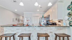 A kitchen with a central island, bar stools, and a microwave. - Waterfront 1BR + Bunk Alcove at The Wharf • Sleeps • Amazing Views • Oasis Pool (Orange Beach)