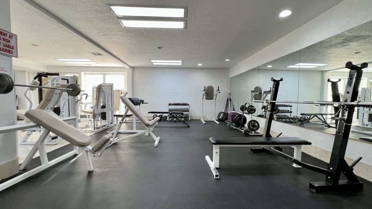 A gym with various exercise equipment, a bench, and a rack of dumbbells.