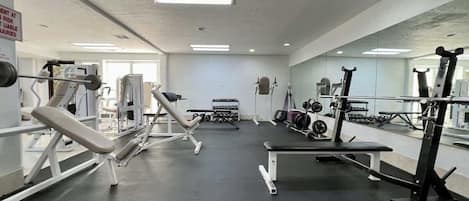 Une salle de sport équipée de divers appareils d’exercice, d’un banc et d’un porte-haltères.
