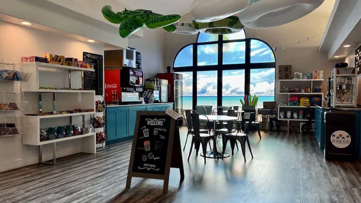 Cafetería con autoservicio, un amplio ventanal y varias estanterías con productos.