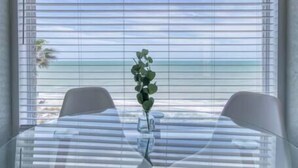 Une table de salle à manger avec un plateau en verre, un vase de fleurs, deux chaises et un luminaire fixé au mur au-dessus.