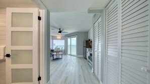 Un pasillo con una puerta blanca, un ventilador de techo y una zona de cocina con refrigerador y estufa.