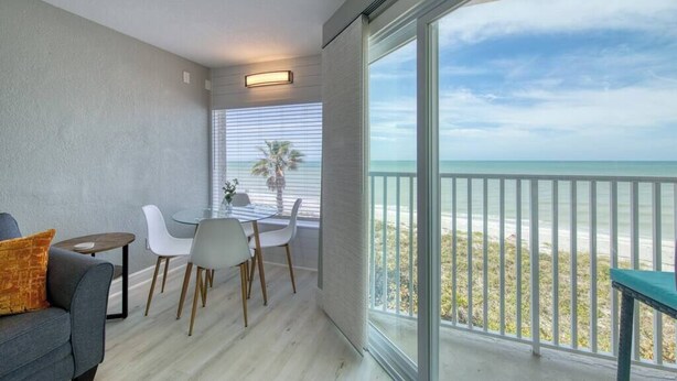 Un balcón con vistas a la playa, un comedor con mesa y sillas, y un sofá.