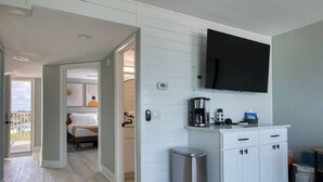 Una habitación de hotel moderna con una cama, un pequeño rincón americano, un televisor montado en la pared y vistas al exterior.