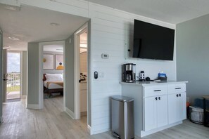 A modern hotel room with a bed, a small kitchenette, a TV mounted on the wall, and a view of the outdoors. - BBC310 Renovated Beachfront Condo W/Pool (Belleair Beach)