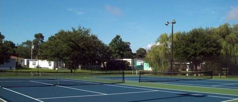 A tennis court with a net, surrounded by trees and buildings.