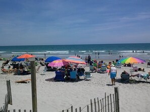 Una playa con varios sombrillas de colores, sillas de playa y gente.
