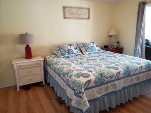 A bedroom with a bed, a nightstand, a lamp, a framed quote on the wall, and a window with curtains.