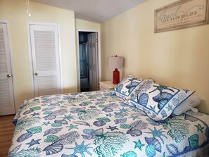 A bedroom with a bed featuring a nautical-themed bedspread, a bedside lamp, and a framed quote on the wall.